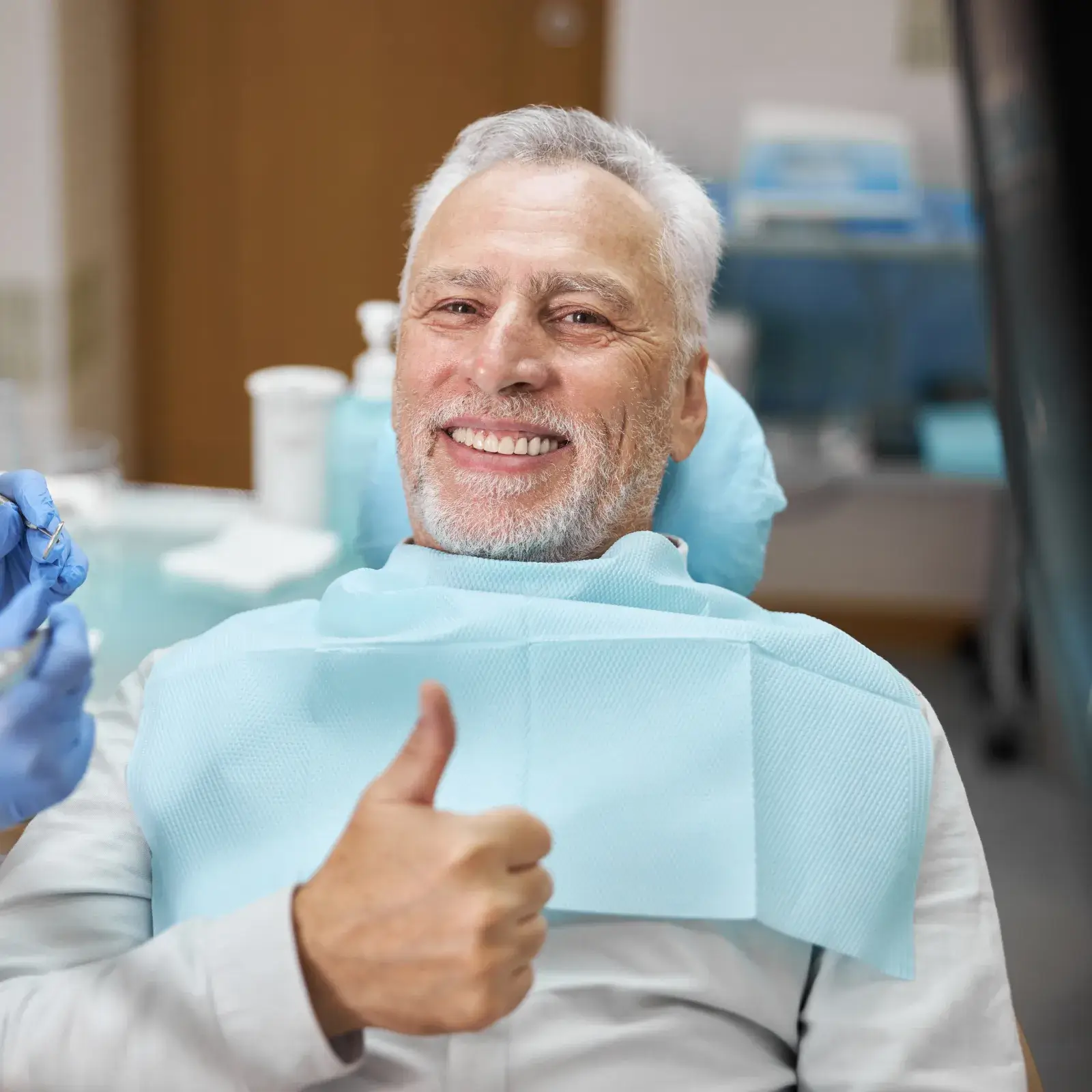 A woman sitting in a dental chair adjusts clear braces on her teeth.