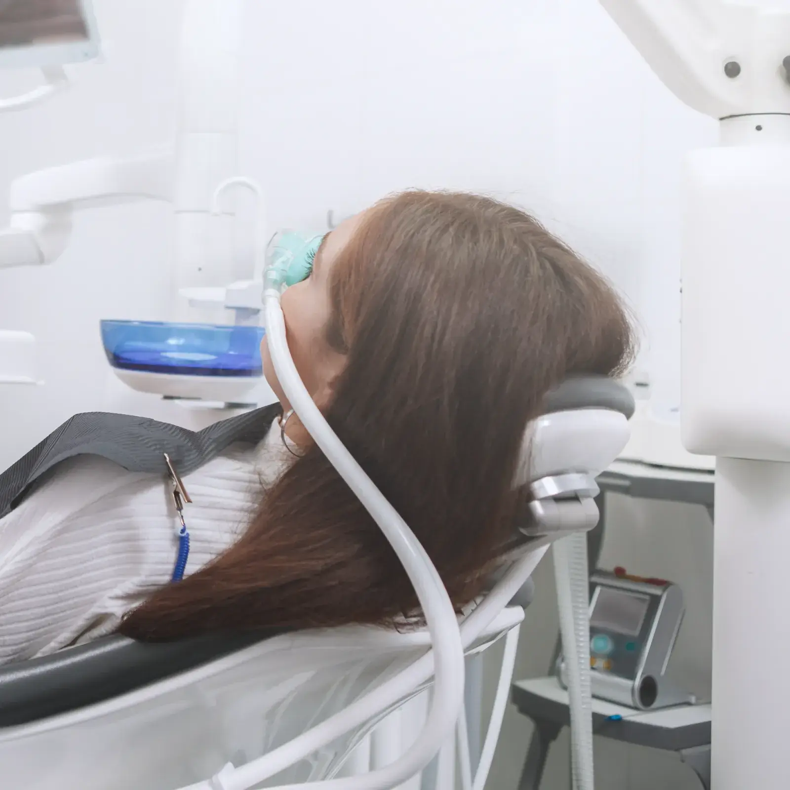 A person lying in a dental chair with a breathing mask on their face.