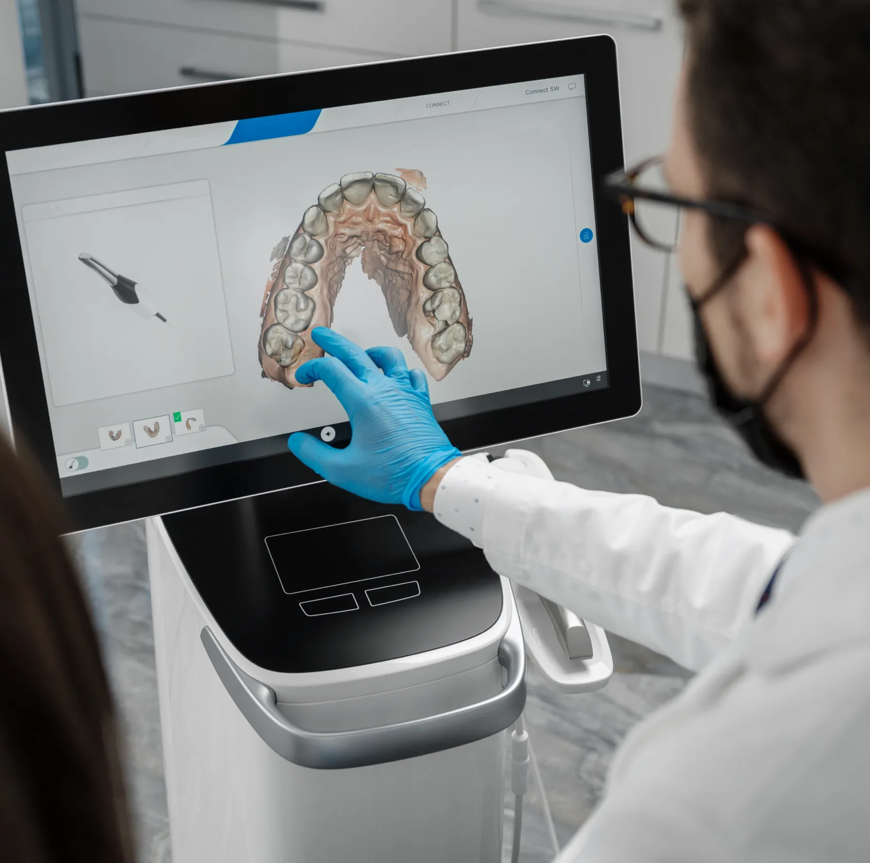 A person wearing gloves uses a touchscreen to view a 3D dental scan of teeth.