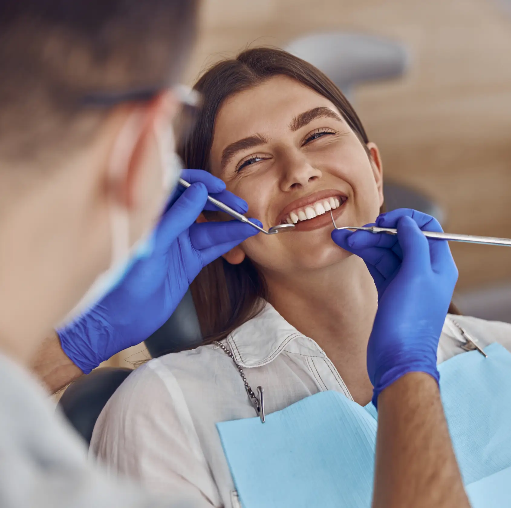 A dentist examines a smiling woman’s teeth using dental tools, while she sits in a clinic chair.