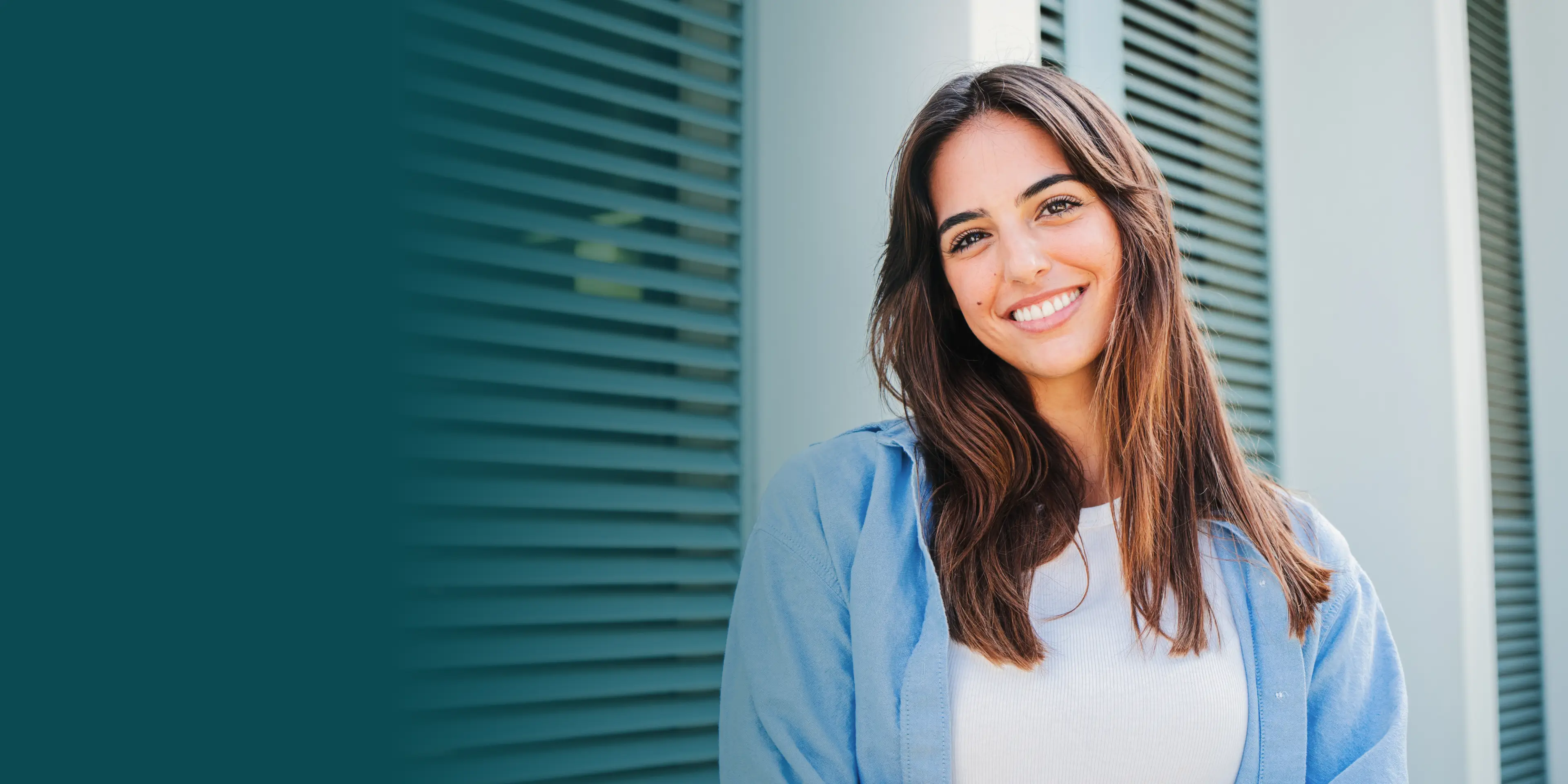 Smiling woman with long hair stands in front of a building with green shutters.