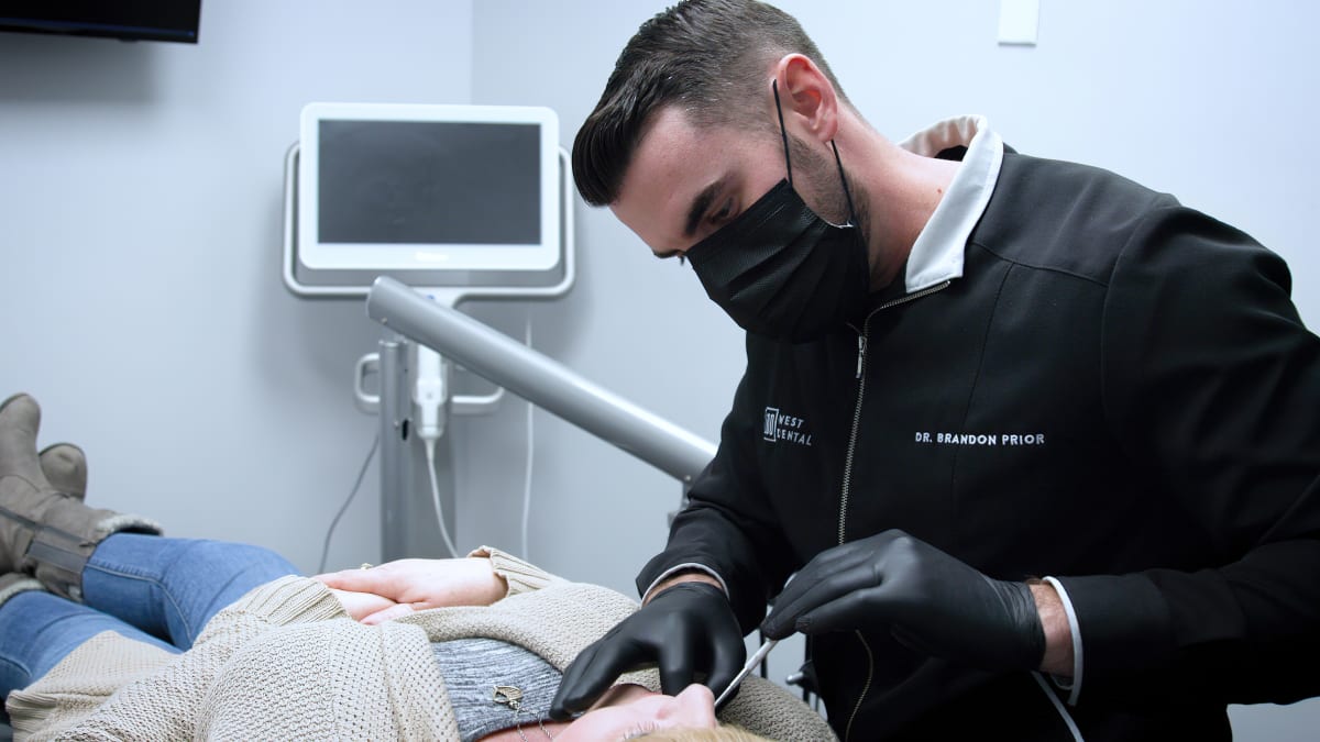Dentist in black gloves examining a patient's teeth during a dental procedure in a clinical setting