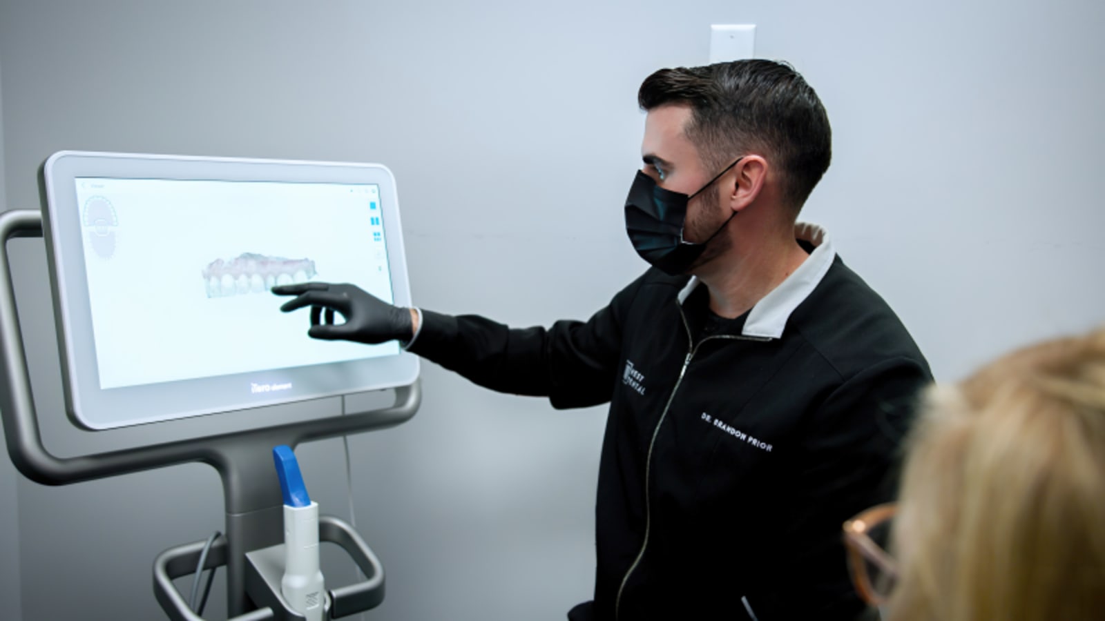 Dentist pointing to digital X-ray or scan image on computer screen during patient treatment