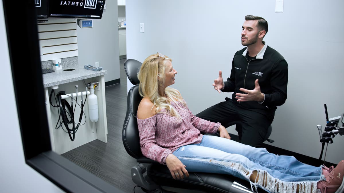 Dental professional demonstrating Invisalign aligners to female patient in modern dental office treatment room.