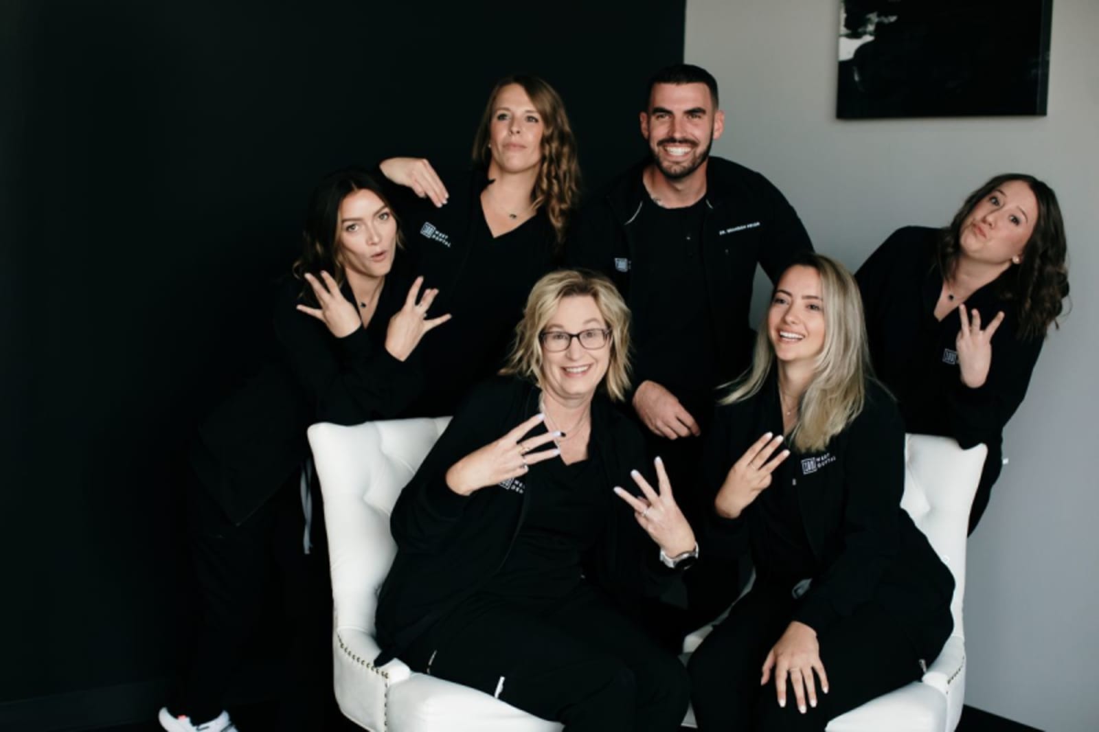 Group portrait of eight smiling dental team members in black clothing against a white background.