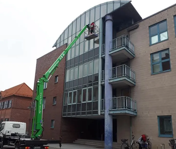 Eine Hebebühne auf der ein Mann steht der eine Fensterwand reinigt