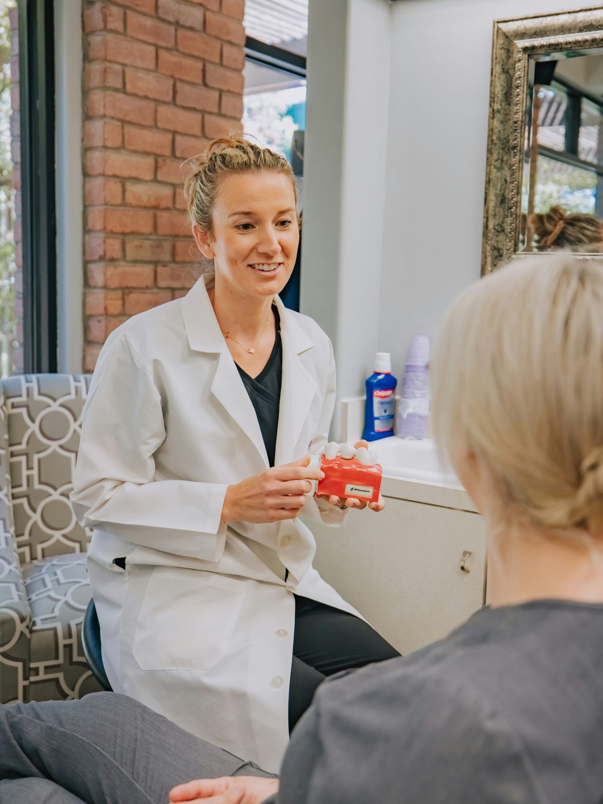 A pharmacist in a white coat talks with a customer in a bright pharmacy consultation corner.