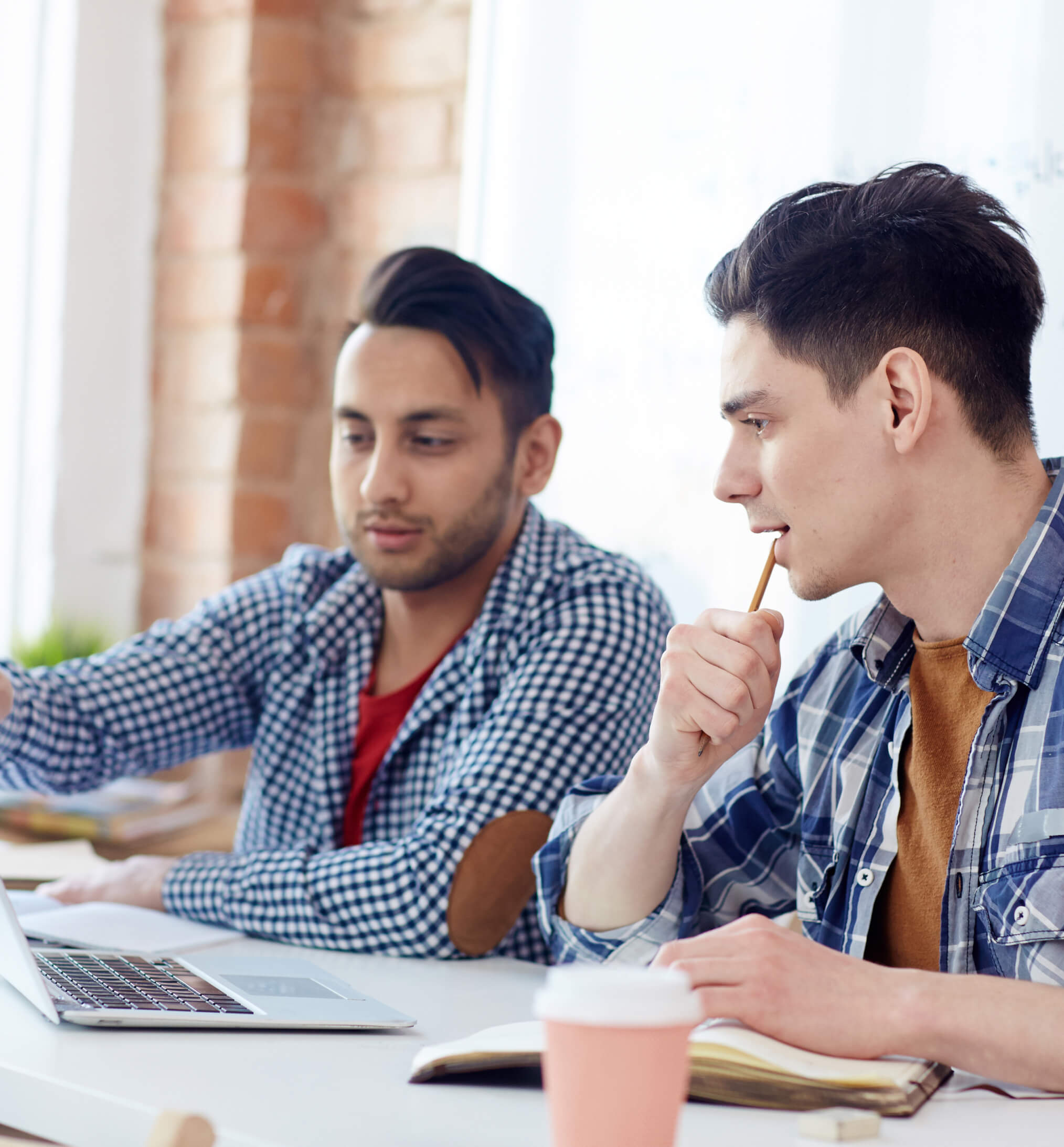 Two men sitting at a table looking at a laptop.