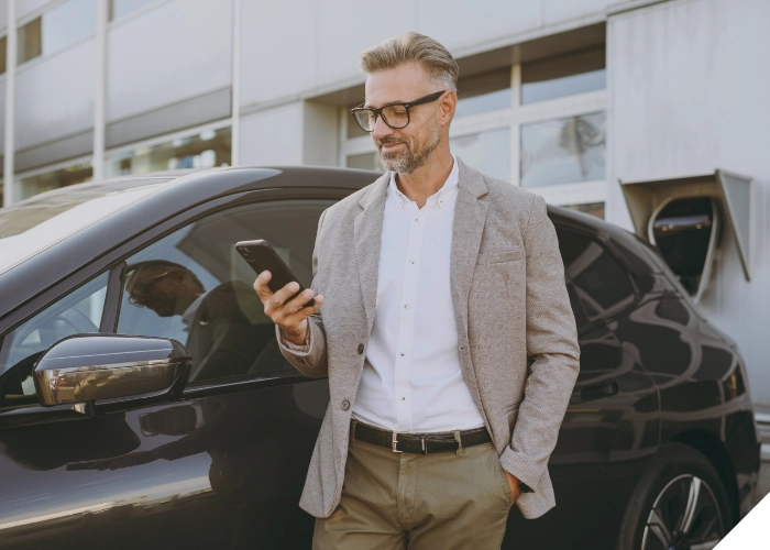 Geschäftsmann nutzt Smartphone neben Firmenfahrzeug