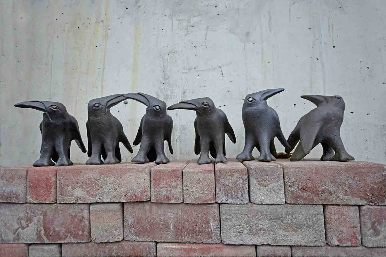 Sechs kleine schwarze Vogelstatuetten auf einem Ziegelsteinmauerwerk vor einer grauen Wand.
