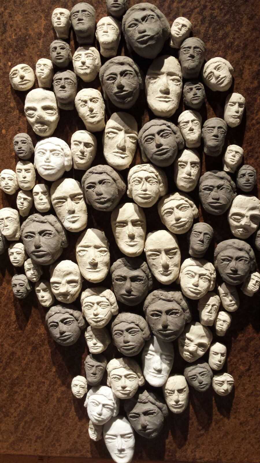 Ansammlung von vielen kleinen, geformten Gesichtern in Weiß- und Grautönen auf rustikalem braunen Hintergrund.