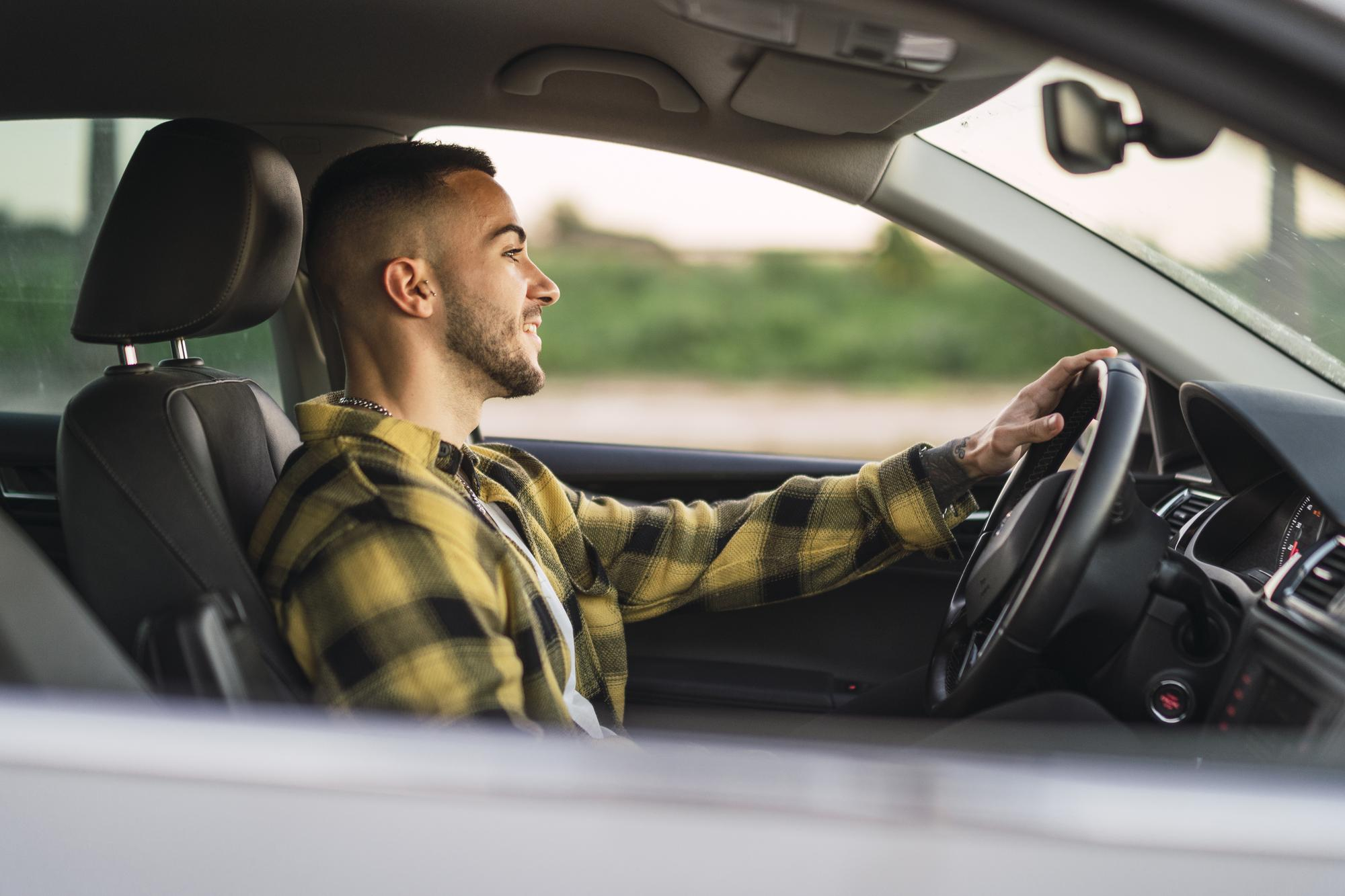 Jeune homme souriant au volant d’une voiture, en pleine leçon de conduite.