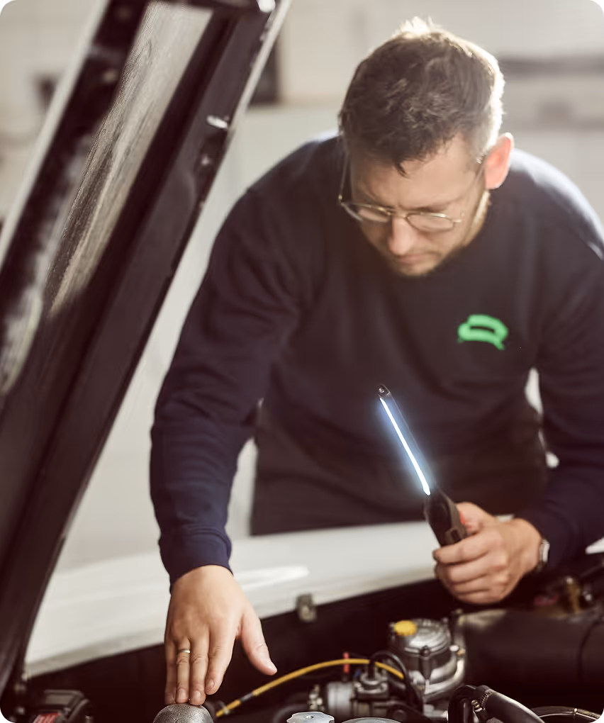 Mitarbeiter blickt in den Motorraum eines Autos zur Erstellung eines Wertgutachtens