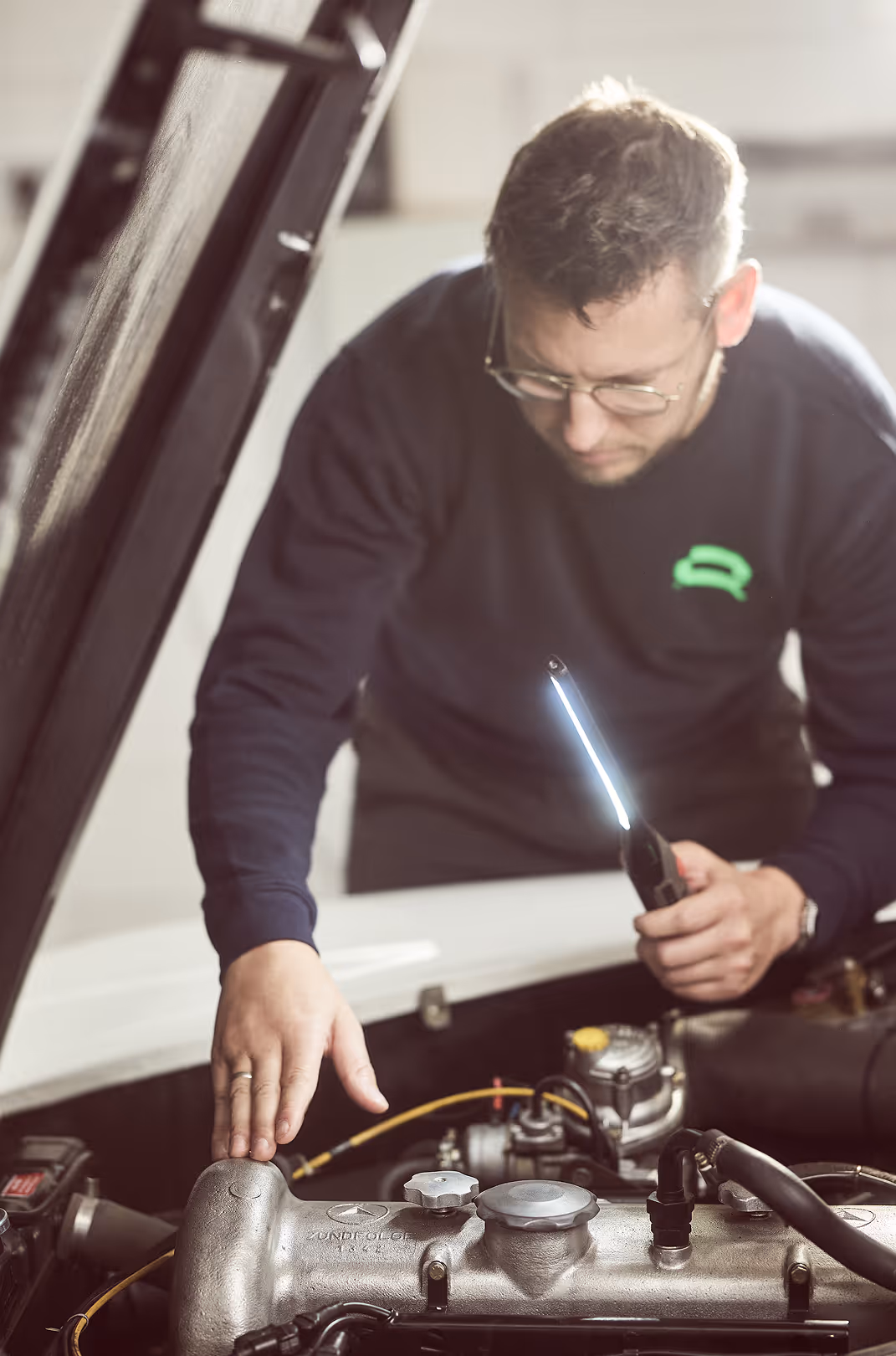 Mitarbeiter blickt in den Motorraum eines Autos zur Erstellung eines Wertgutachtens