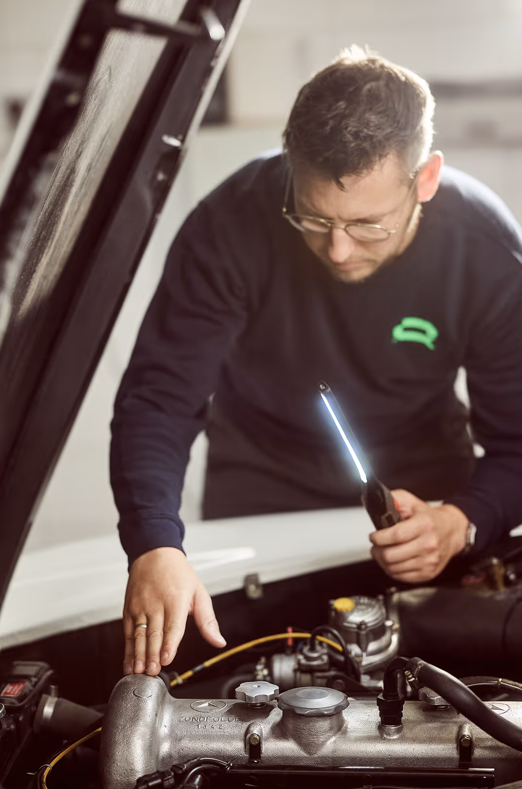 Mitarbeiter blickt in den Motorraum eines Autos zur Erstellung eines Wertgutachtens