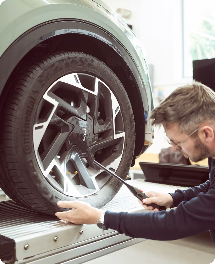 Mitarbeiter untersucht den Reifen eines Autos in der Schadenprüfhalle