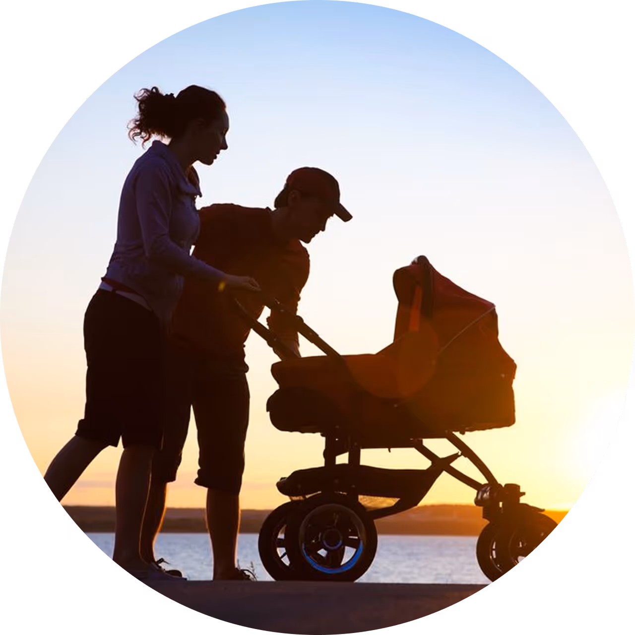 Parents out for a walk with stroller near water during sunset.