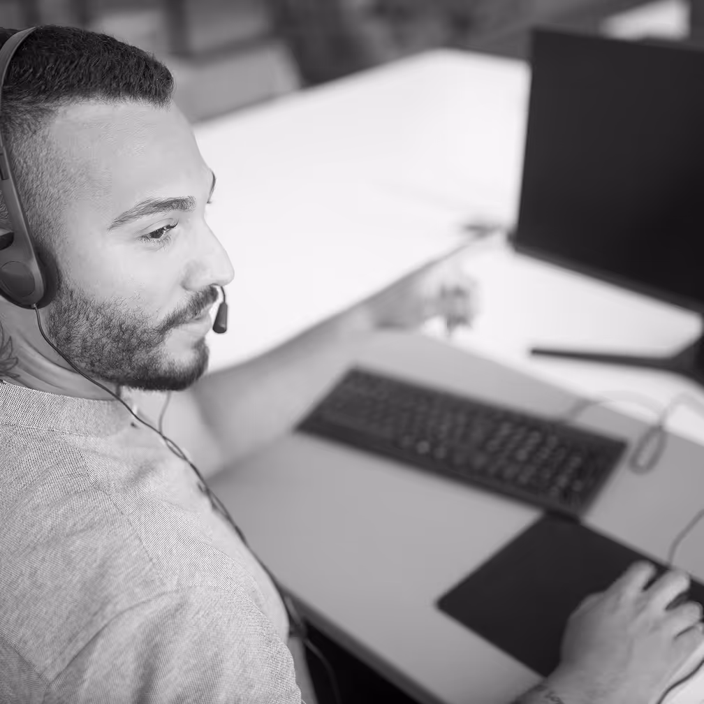 Employee on a headset phone at his desk, pointing at his computer screen