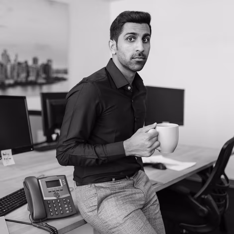 Man drinking coffee at a desk with a desk phone in the background