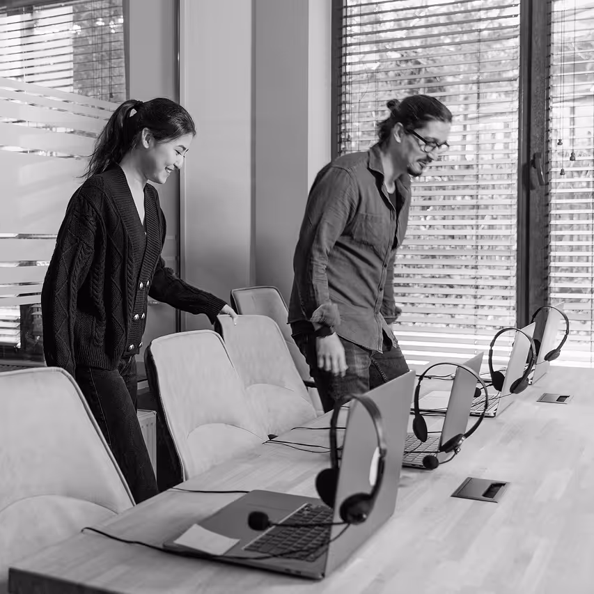 Two employees taking a seat at their desks with laptops and headsets