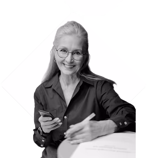 Teacher smiling at camera, holding a cellphone while jotting down some notes