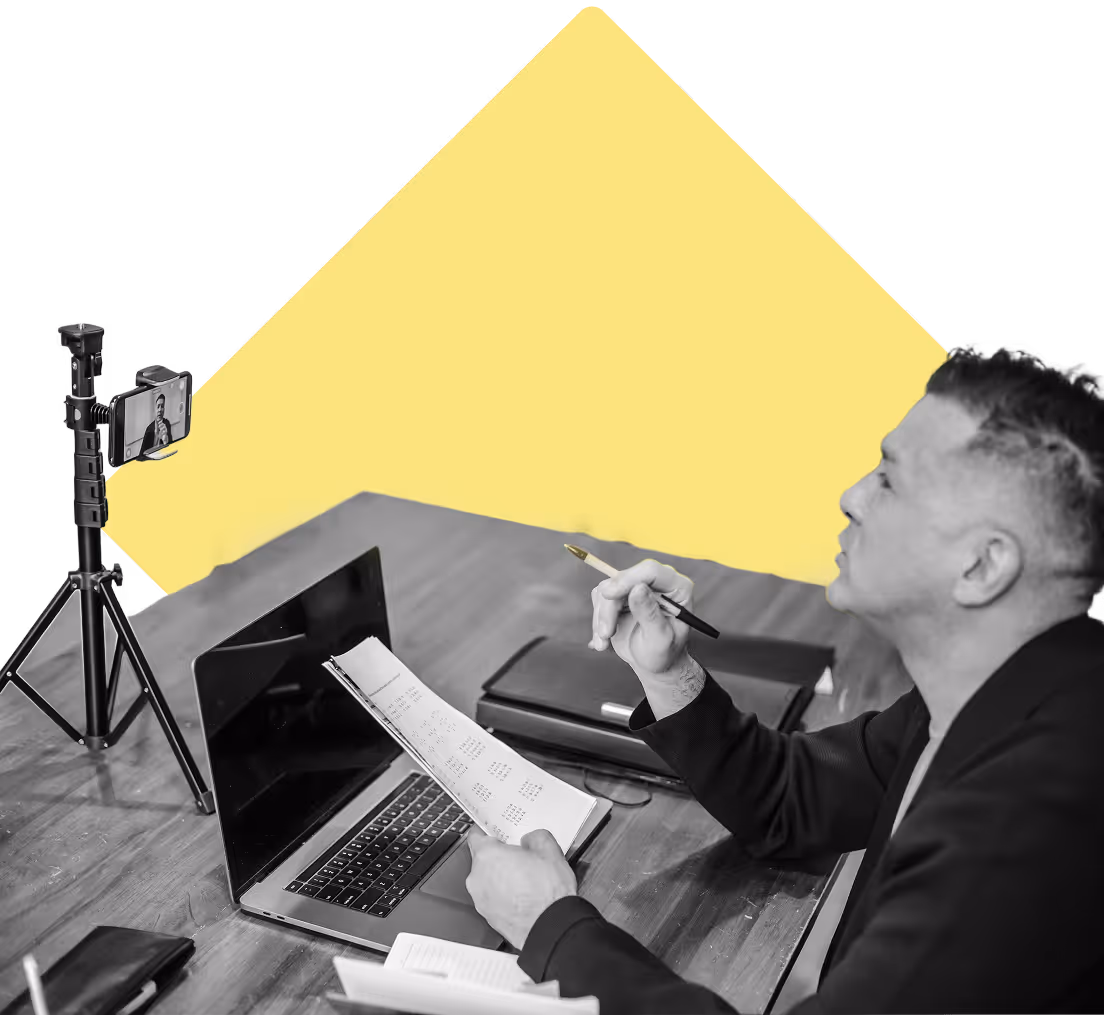 Man teaching a class remotely with phone stand set up, laptop, and class curriculum in hand