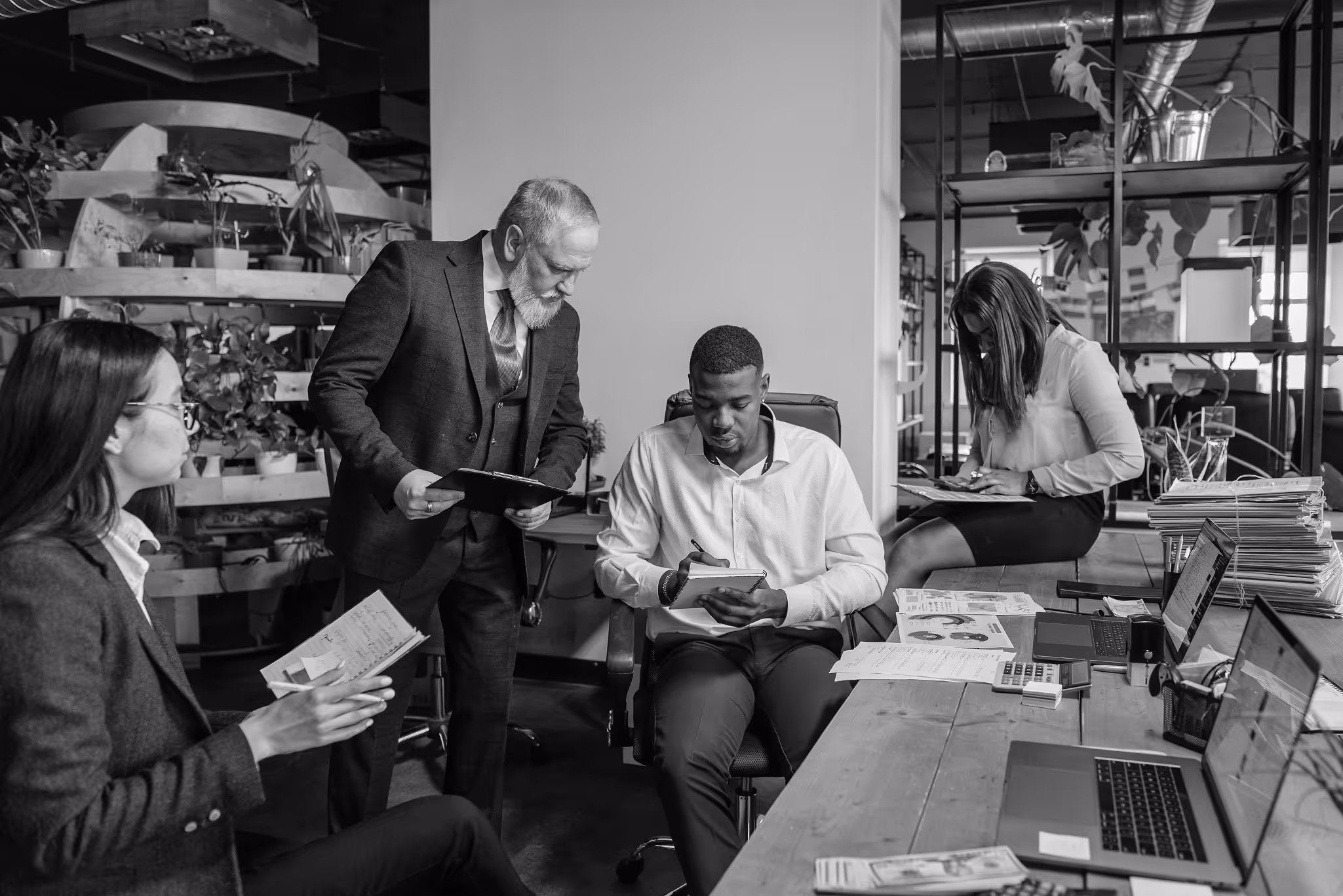 Four professionals at a law firm discussing documents and working with laptops at a wooden table.