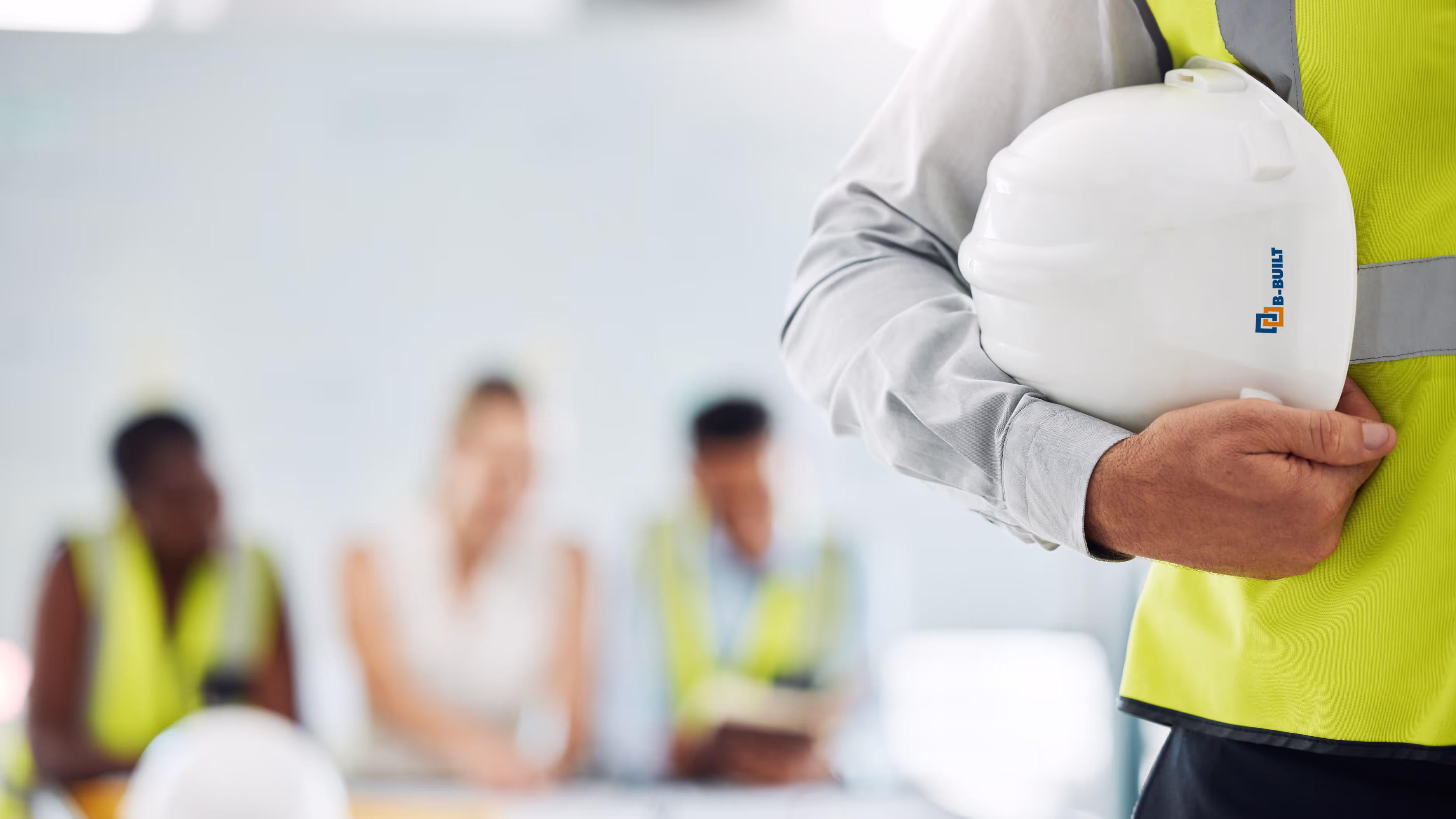 Person holding a white hard hat and wearing a high-visibility safety vest at a construction site.