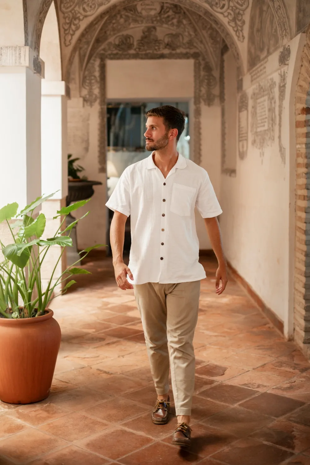A man in a white shirt is walking down a hallway.