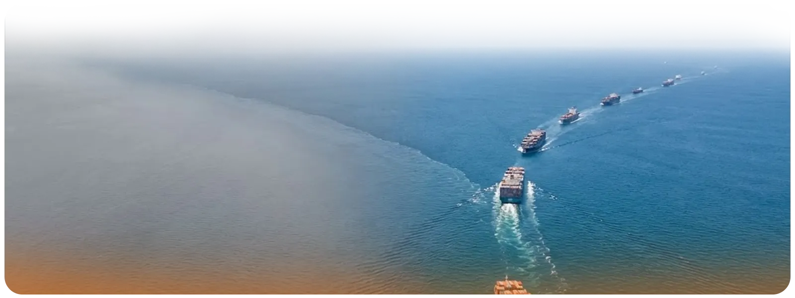Line of container vessels traveling across calm ocean waters, reflecting a softer rate outlook.
