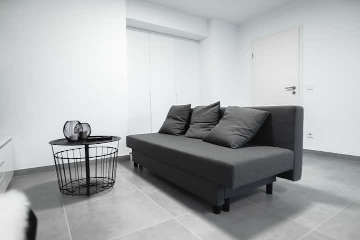 Sala com sofá cinzento e almofadas claras, luz natural