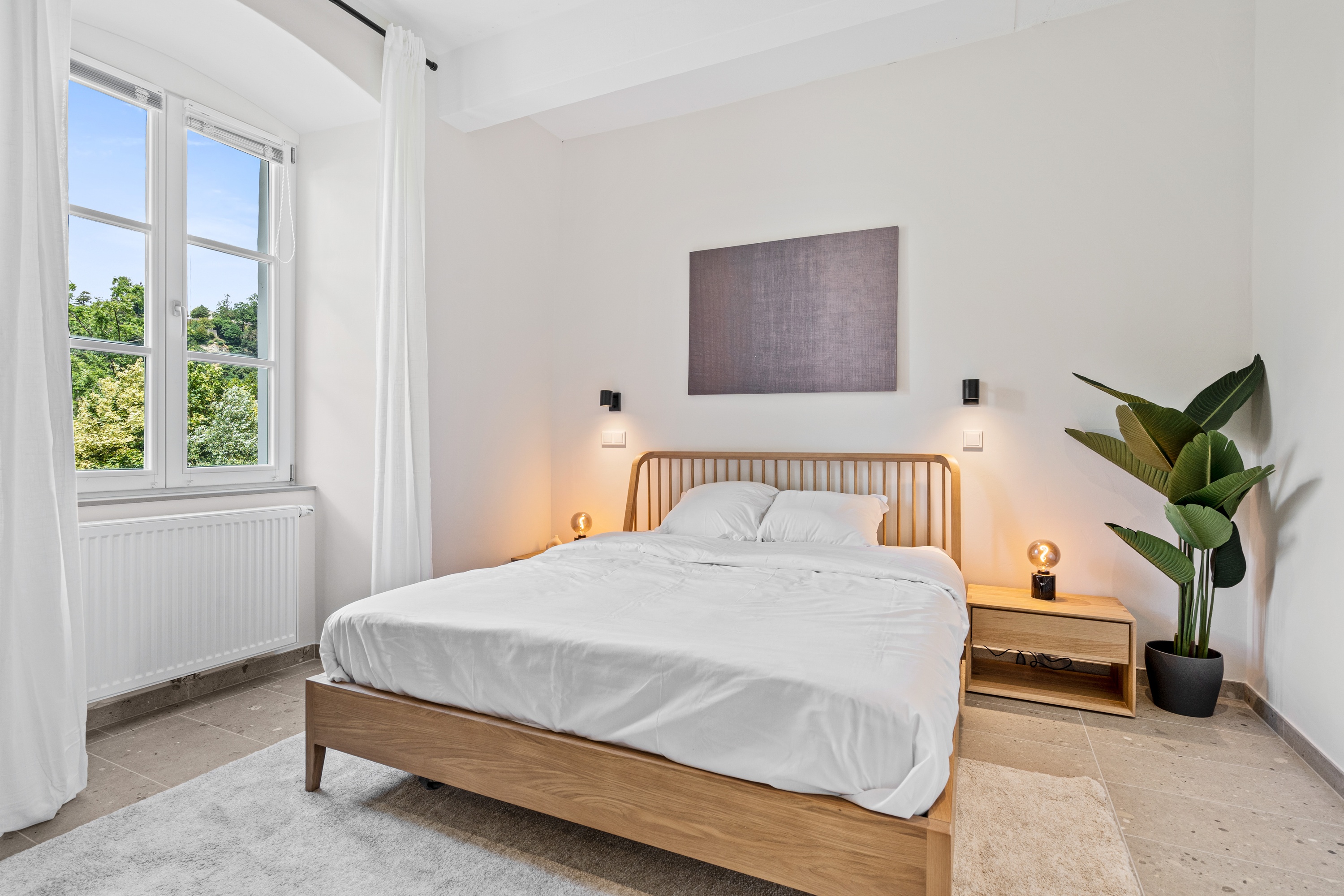 Quarto com cama de casal, luz natural e planta decorativa