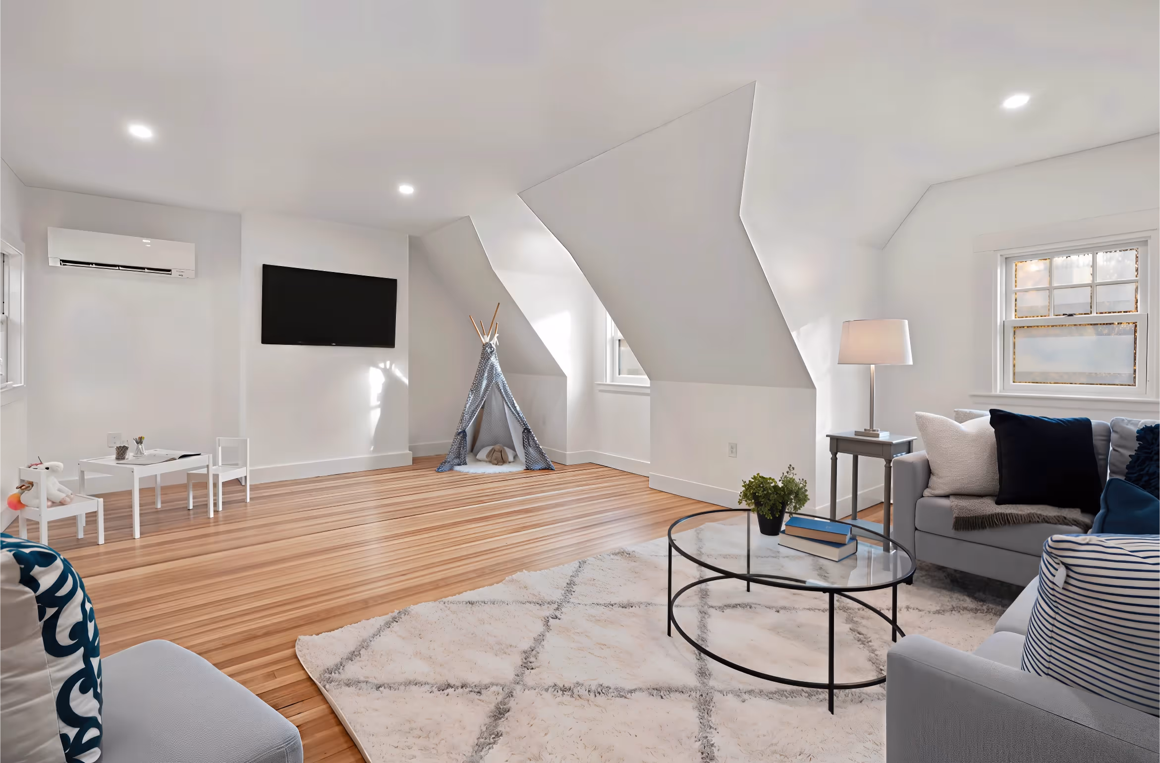 Bright, modern living room with a play area, teepee, TV, sofa, round coffee table, and large rug.