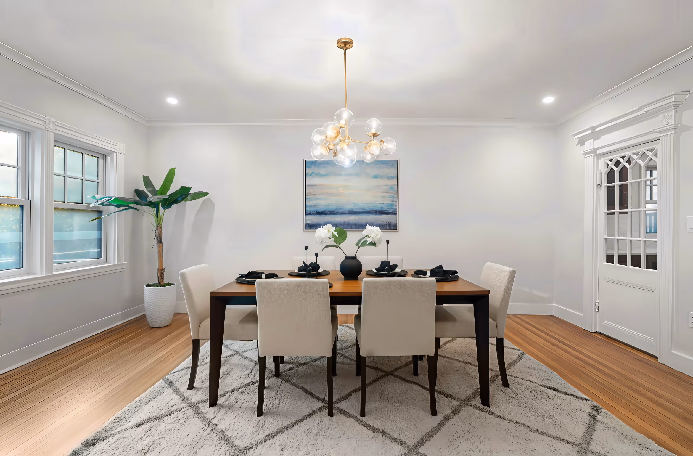 Modern dining room with six white chairs, wooden table, abstract wall art, and a hanging light fixture.