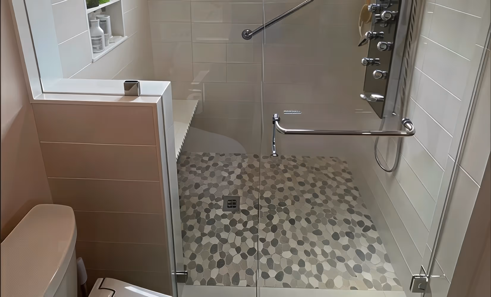 Modern accessible shower with a glass door, grab bars, bench, and stylish shower tile installation on the patterned floor.