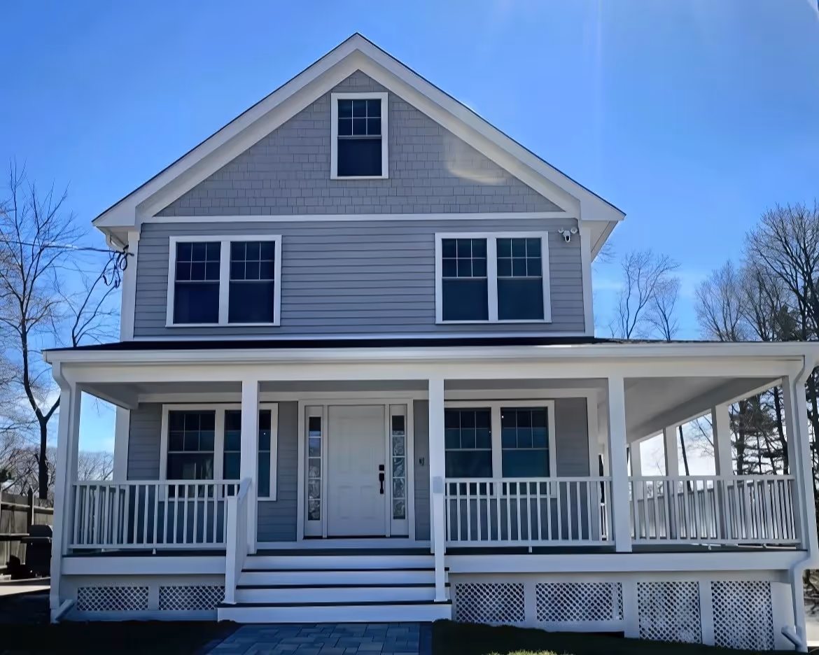 A two-story gray house with a white porch, steps, and railings, under a clear blue sky.