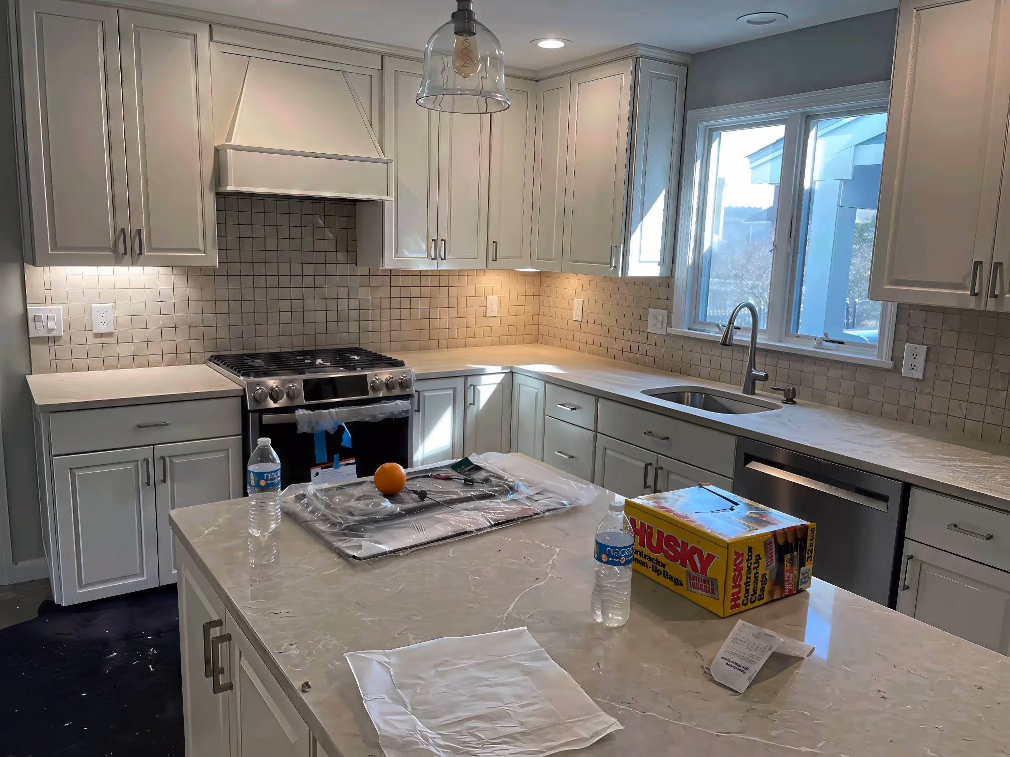 Modern kitchen remodeling in Boston with white custom cabinetry, marble island, stove, sink, and cleaning supplies on the counter.
