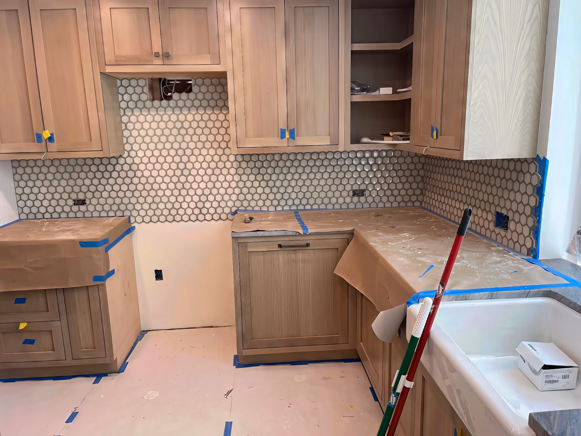 A kitchen remodeling project underway with custom cabinetry, hex tile backsplash, and surfaces covered for protection.