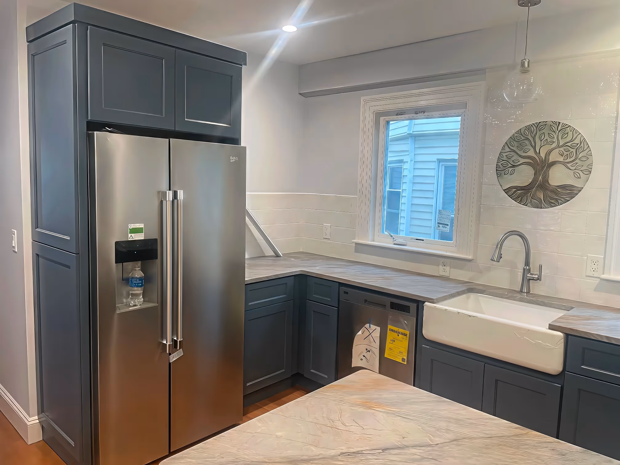 Modern kitchen with custom cabinetry in gray, stainless steel appliances, and a tree wall art above the sink.