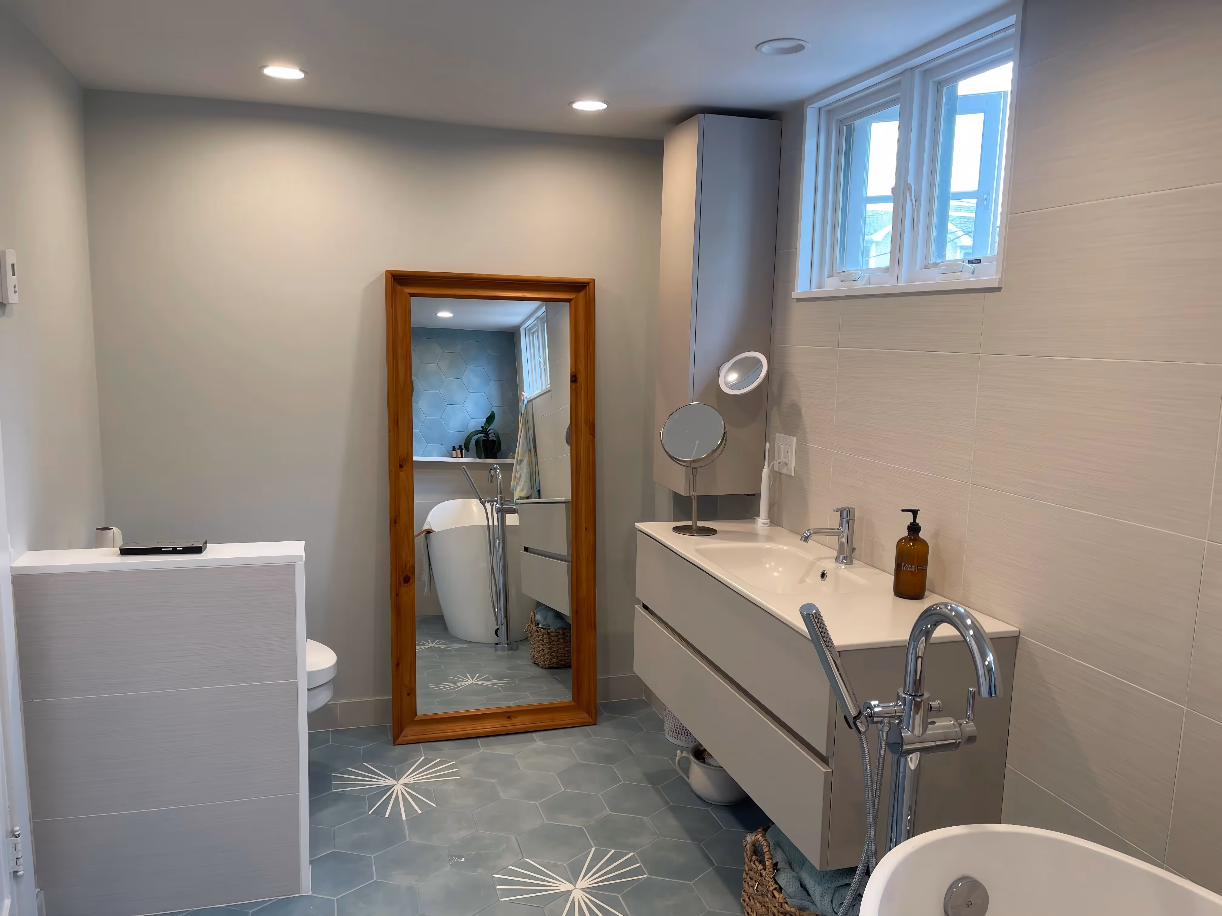 Modern, luxurious bathroom featuring a freestanding tub, large mirror, hexagonal tile floor with white accents, and walk-in showers for a spa-like experience.