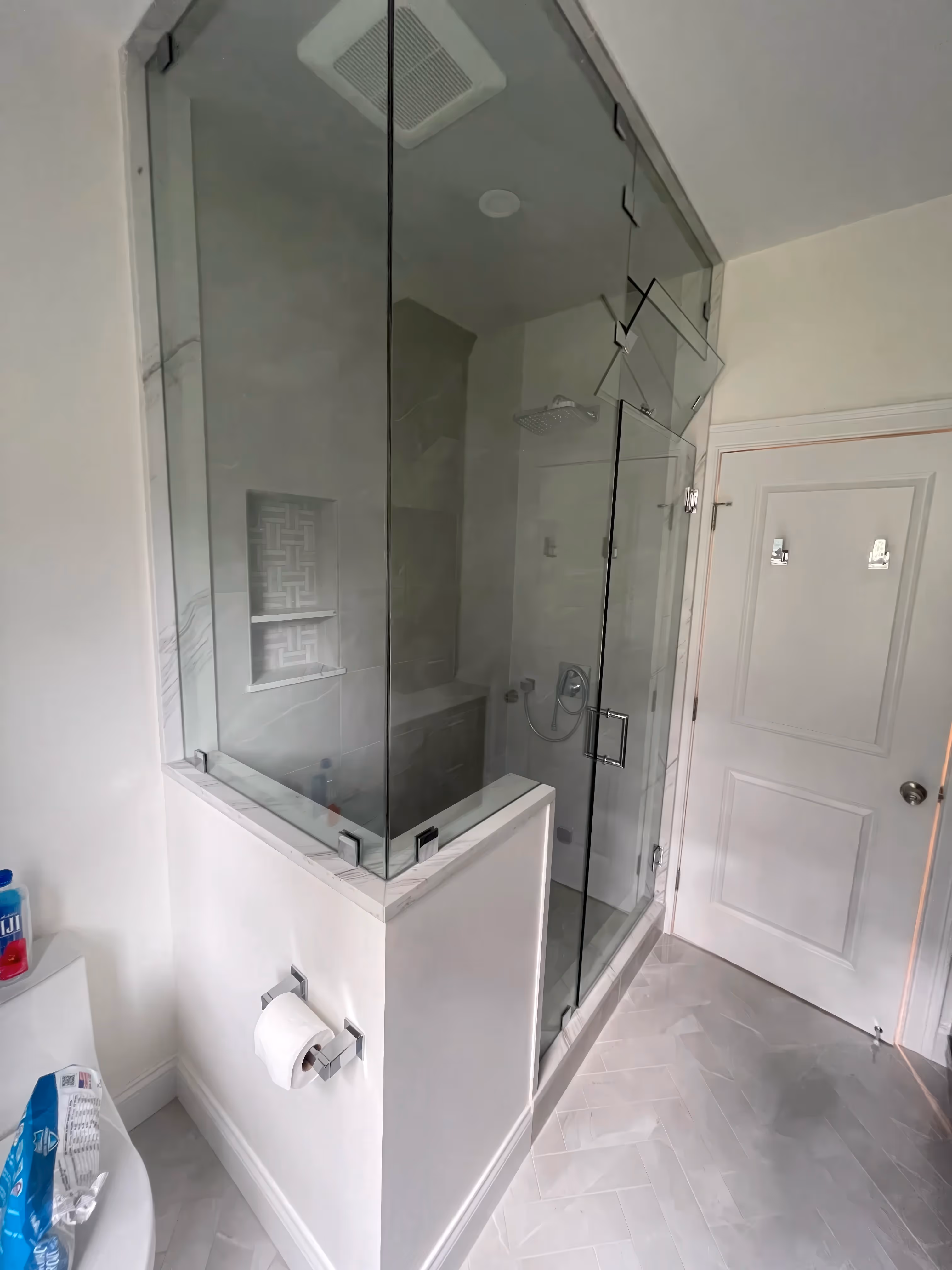 Modern glass-enclosed walk-in shower with bench and rainfall showerhead enhances this white bathroom, showcasing elegant bathroom design.