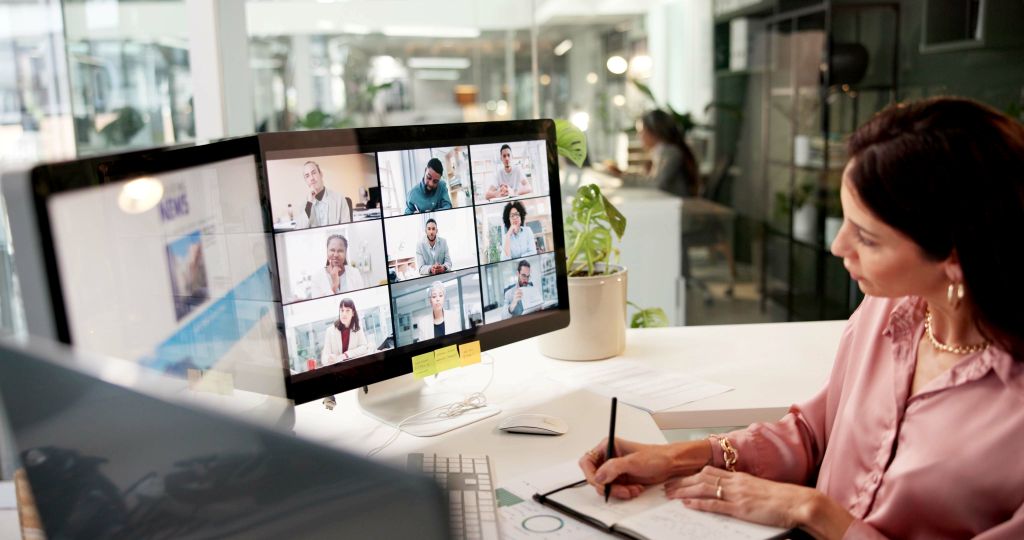 Woman participating in virtual video conference with multiple colleagues on screen