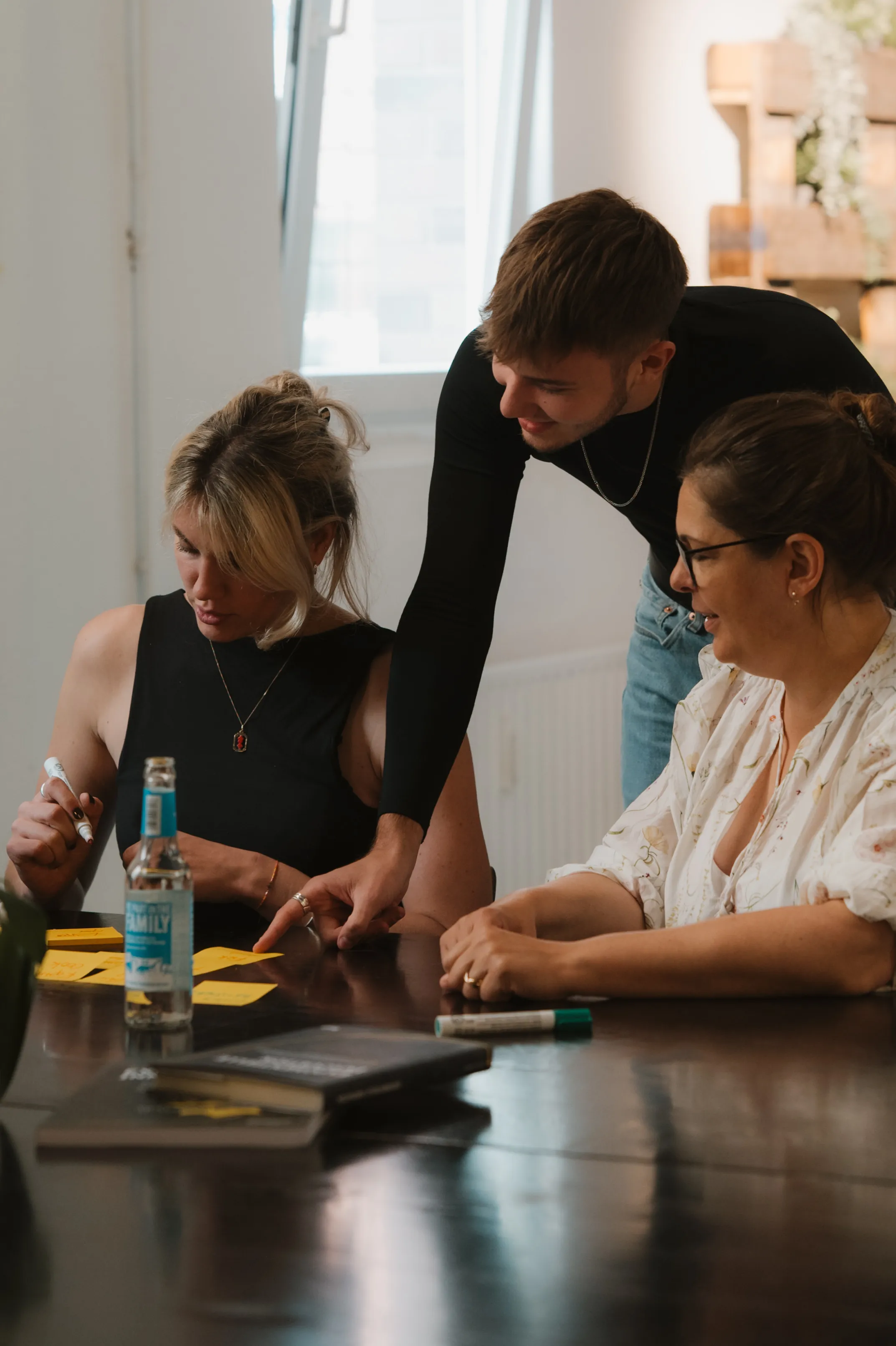 Drei Personen diskutieren und schreiben Notizen auf Zetteln an einem Tisch in einem hellen Raum.