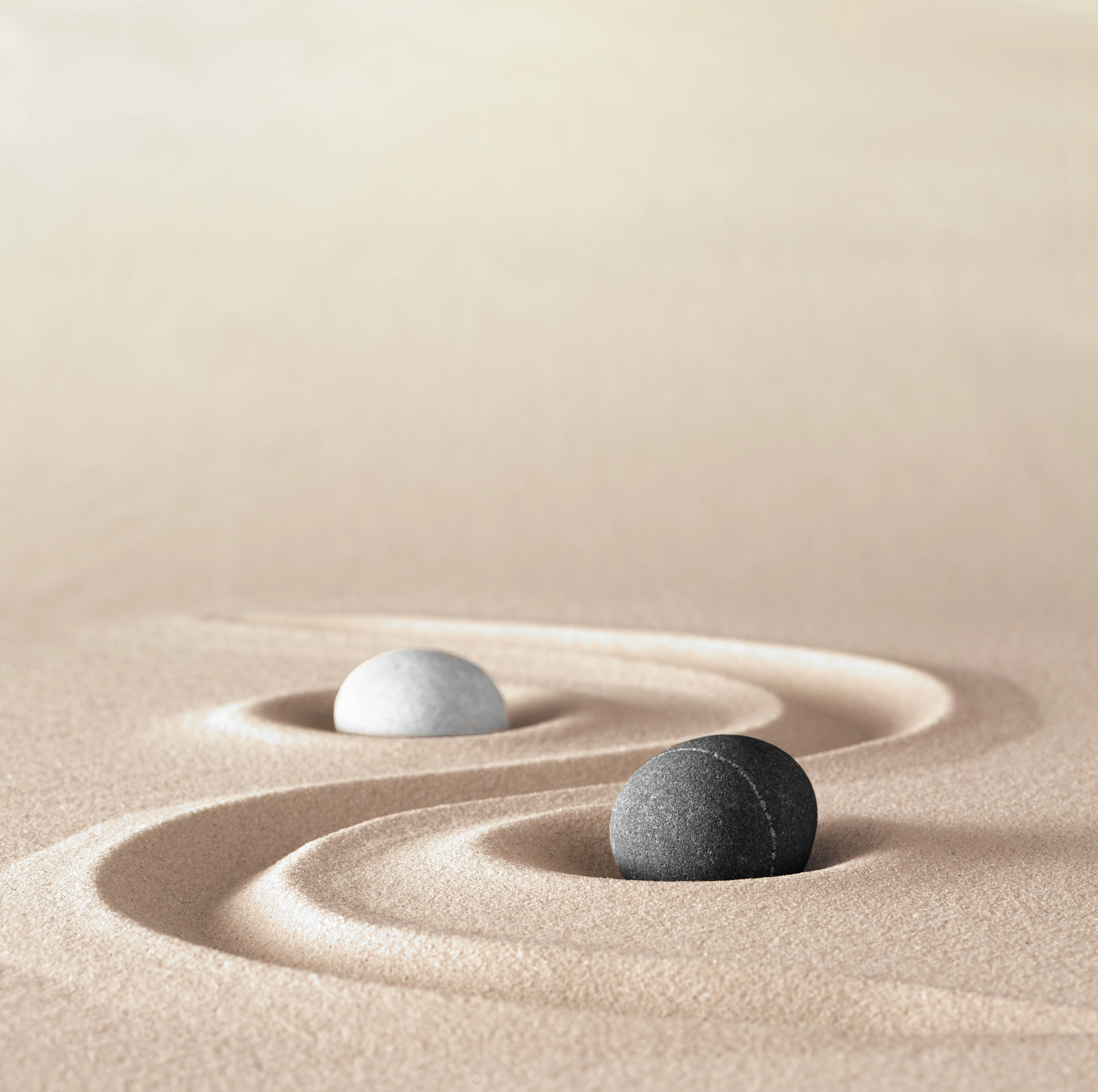 Zwei Steine in harmonischem Sandmuster – Symbol für Yin und Yang in der ruhigen, meditativen Praxis des Yin Yoga.