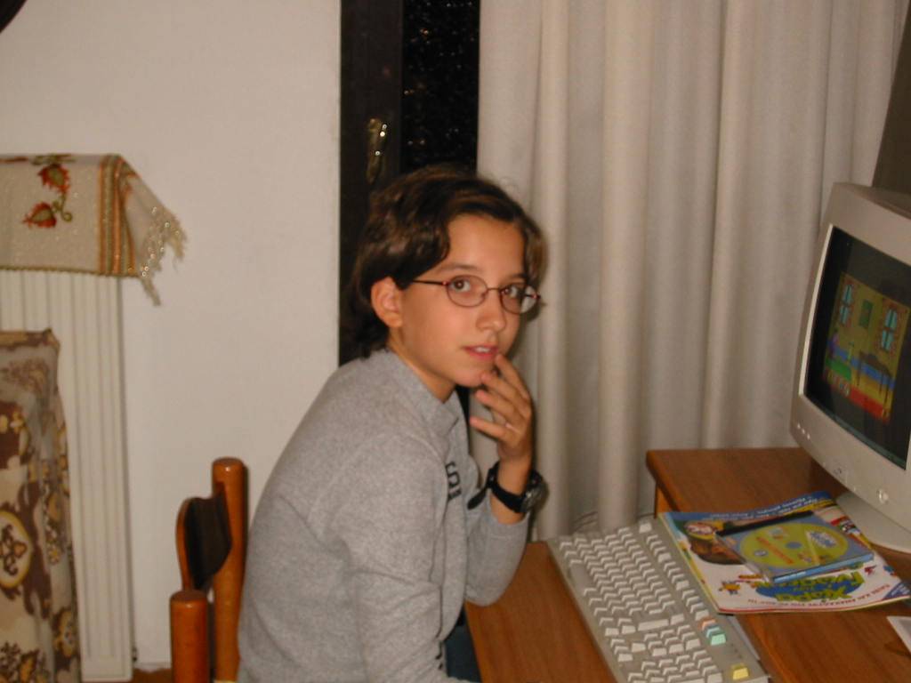 Image of young Konnie sitting in front of a desktop computer, looking at the camera
