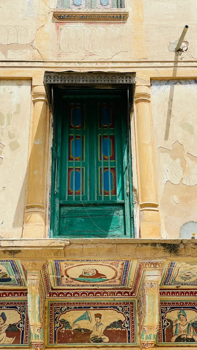 Vintage wooden door framed by hand-painted murals and fading lime plaster walls