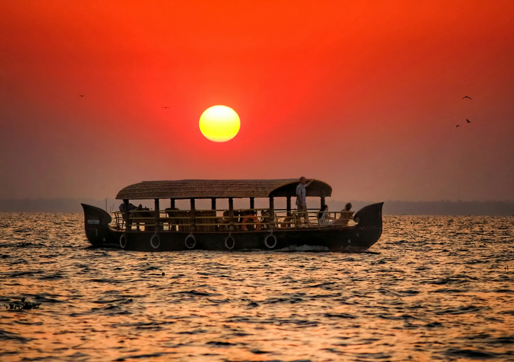 Houseboat sailing across calm backwaters at sunset with golden reflections