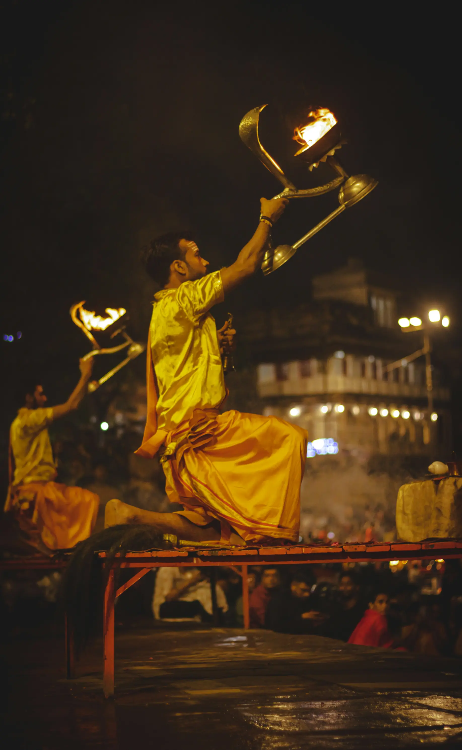 Hindu priest mid-ritual holding a large aarti lamp during the evening ceremony on the ghats