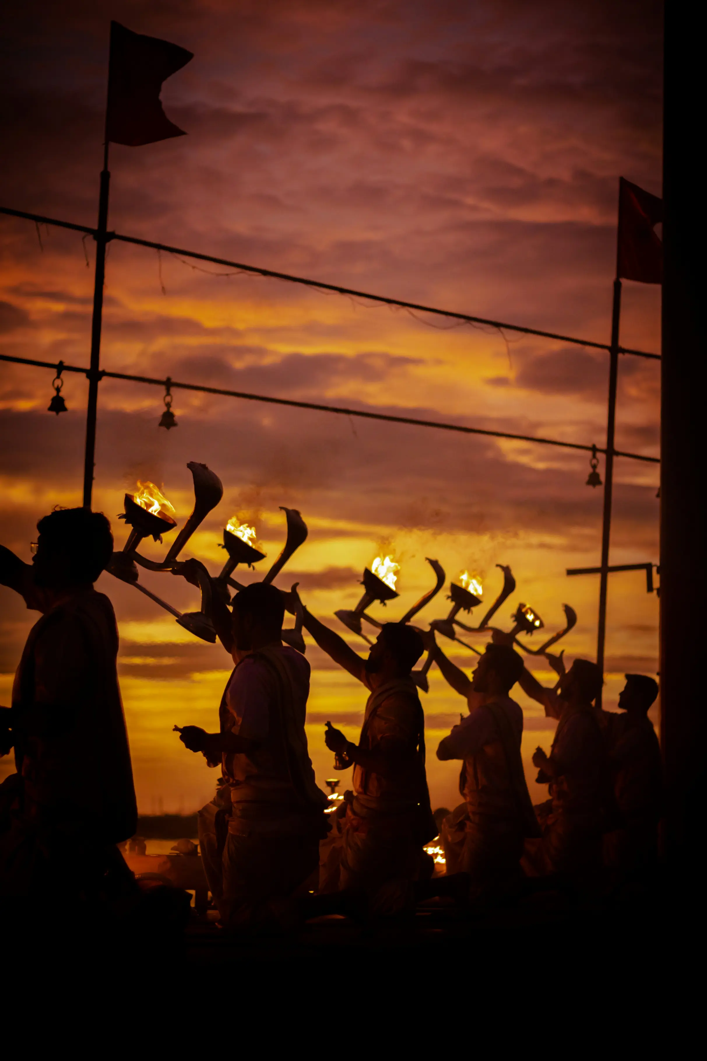 Priests performing Ganga aarti at sunset with flaming lamps against a dramatic sky in Varanasi