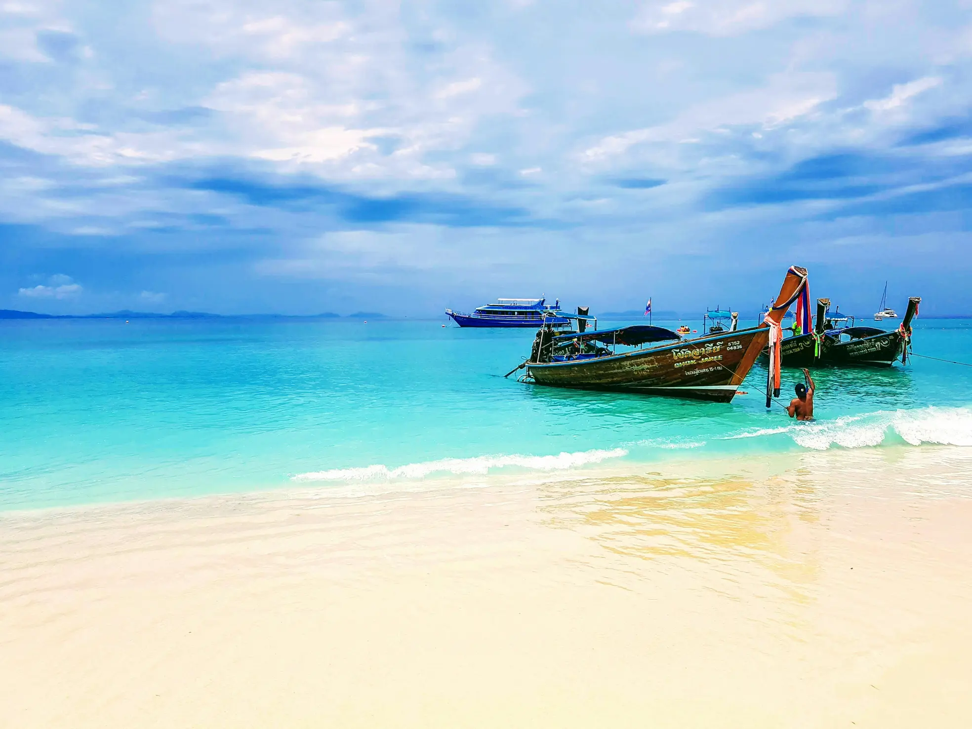 Longtail boats anchored along a white sand beach with clear blue water